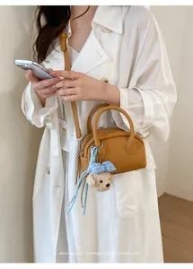 Detailed view of the stylish brown leather Boston bag with a cute bear plush charm.
