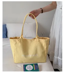 Detail shot of a yellow canvas tote bag with letter print, shown in a simple bedroom scene.