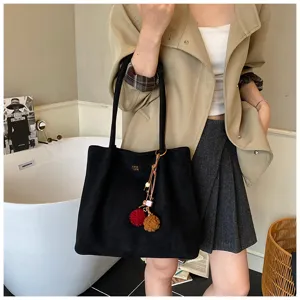Black suede tote bag detail view, showing soft texture and cute pom-pom keychain accessory.