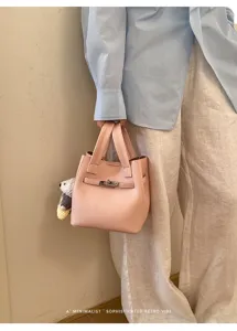Pink leather bucket bag with top handle and metal lock charm, minimalist daily handbag.