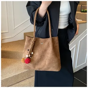 Close-up detail of the brown suede tote bag with cute pom-pom pendant in indoor scene.