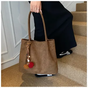 Close-up detail shot of the brown suede tote bag featuring a chic charm on the stairs.