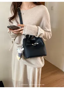 Black leather bucket shoulder bag with metal lock closure and chic minimalist retro design style.