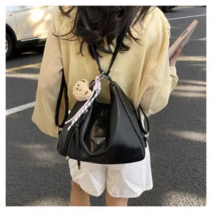 Detailaufnahme eines schwarzen Leder-Rucksacks mit Dreiecks-Logo und süßem Bären-Anhänger.