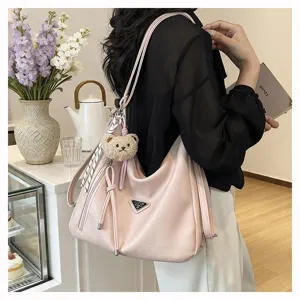 Stilvolle rosa Damen Schultertasche mit Bärenanhänger und metallenem Dreieckslogo.