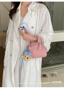 Detailed shot of a stylish pink mini Boston bag with a cute blue bow bear pendant accessory.