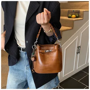 Detailed shot of retro brown leather bucket bag with metal lock closure and braided handle.