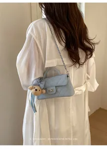 Detailed shot of a stylish light blue quilted shoulder bag with chain strap and cute bear charm.