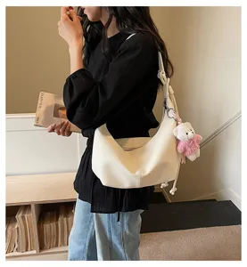 Detailed shot of a stylish white hobo shoulder bag with a cute bear pendant, daily casual wear.