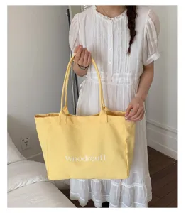 Detailed view of the yellow canvas tote bag featuring front letter print and comfortable handles.