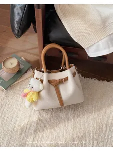 Elegant two-tone women handbag with top handle, cute bear pendant, and stylish bucket design.