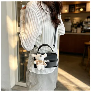 Detail view of black textured crossbody bag with cute plush dog keychain and metal lock.