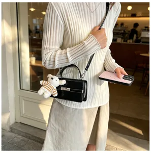 Stylish black patent leather women handbag detail view featuring a cute bear plush pendant.