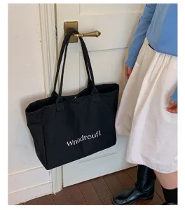 Detail shot of black canvas tote bag with white letter print hanging on door handle.