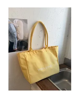 Detailed view of yellow canvas tote bag with shoulder straps and white printed text design.