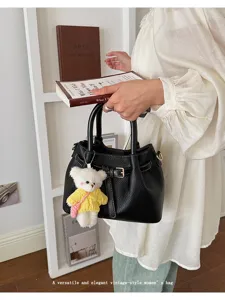Black leather tote bag with cute white bear plush pendant and chic buckle strap detail.