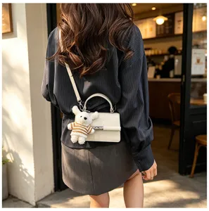 Detail shot of trendy women's PU leather crossbody bag with cute plush bear pendant accessory.