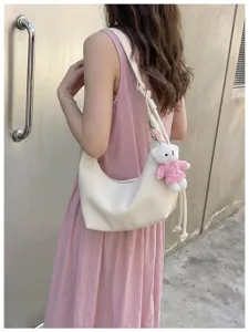 Close-up detail of stylish casual dumpling shoulder bag with cute bear pendant in off-white.