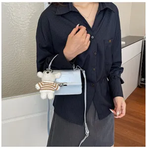Chic light blue patent leather crossbody bag with cute plush bear charm, stylish detail.