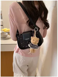 Detail view of black shoulder bag with star pattern, leather flap, and cute teddy bear charm.