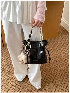 Black patent quilted bucket bag with chain strap and cute plush puppy keychain accessory.