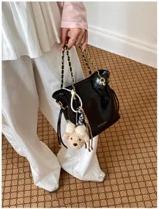 Close-up detail of a black patent leather quilted shoulder bag with chain strap and cute bear charm.