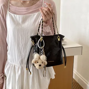 Chic black quilted bucket bag with gold chain strap, drawstring, and cute bear plush pendant.