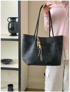Detail shot of the black textured tote bag with a wooden bead charm and thin straps.