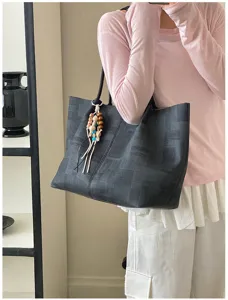 Detail view of a minimalist dark tote bag featuring wooden bead pendant, casual style.