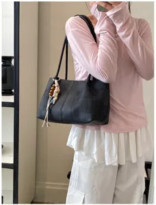 Detail shot of a minimalist black shoulder tote bag with cute bead pendant for women.