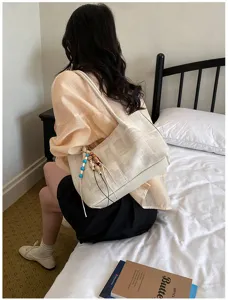 Close-up of casual beige canvas tote bag with beaded charm detail in cozy bedroom.