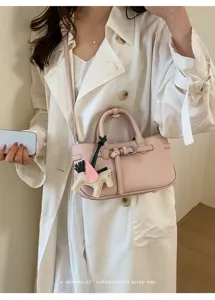 Detailed shot of stylish pink leather crossbody bag with wing charm and retro aesthetic.