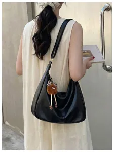 Detail shot of black slouchy hobo shoulder bag with fuzzy charm on model's back, casual.