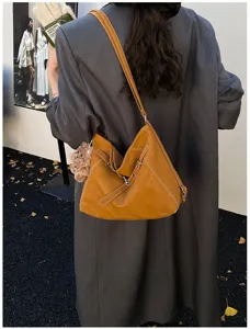 Close-up detail of stylish brown leather hobo shoulder bag with contrast stitching and bear charm.