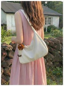 White slouchy shoulder bag detail outdoors, soft leather hobo style with cute pendant.
