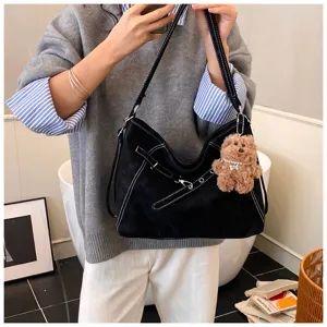 Black vintage suede shoulder bag detail showing white contrast stitching and cute bear charm.