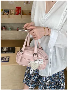 Detail shot of a pink bowling handbag with pearl bow charm, held by model in daily scene.