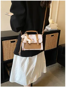 Stylish women's crossbody handbag with chic color block design and cute pendant charm.
