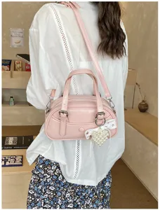 Detail view of stylish pink bowling handbag with pearl bow pendant and shoulder strap.