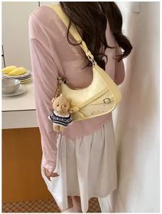 Detail shot of a stylish light yellow shoulder bag with star pattern and cute bear charm pendant.