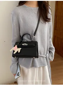 Detailweergave van stijlvolle zwarte Kelly handtas met paardenhanger en grijze trui gedragen.