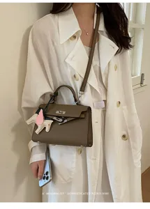 Detailopname van een bruine lederen tas met bedel in minimalistische retro-stijl.