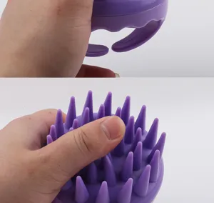 Nahaufnahme einer Hand, die eine lila Silikon-Kopfhautmassagebürste mit Borsten hält.