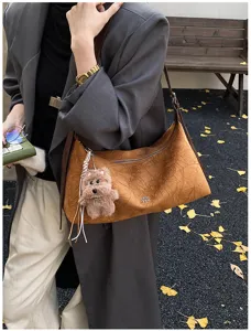 Detailed view of brown suede underarm shoulder bag featuring adorable plush bear charm.