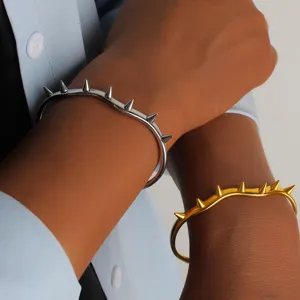 Bracciale rigido aperto con rivetti conici in acciaio al titanio, dettaglio stile punk.