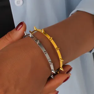 Bracciale rigido acciaio titanio con borchie coniche, dettaglio, stile rock minimalista oro argento.