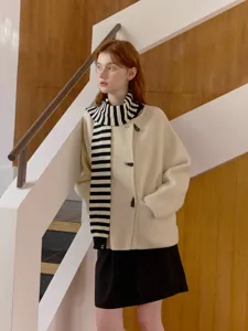 Detailed shot of stylish cream white wool coat paired with black and white striped scarf.