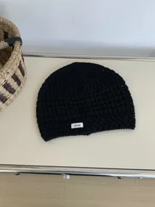 Detail shot of a black knitted hollow-out beanie hat with a small REMAKE label for casual wear.