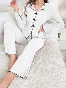 White ribbed pajama set with black bow details shown on a model sitting on a bed