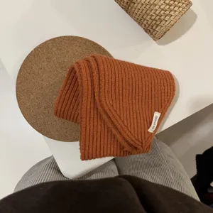 Orangefarbenes Strick-Dreiecktuch im Detail, zeigt weiche Textur und Markenetikett.